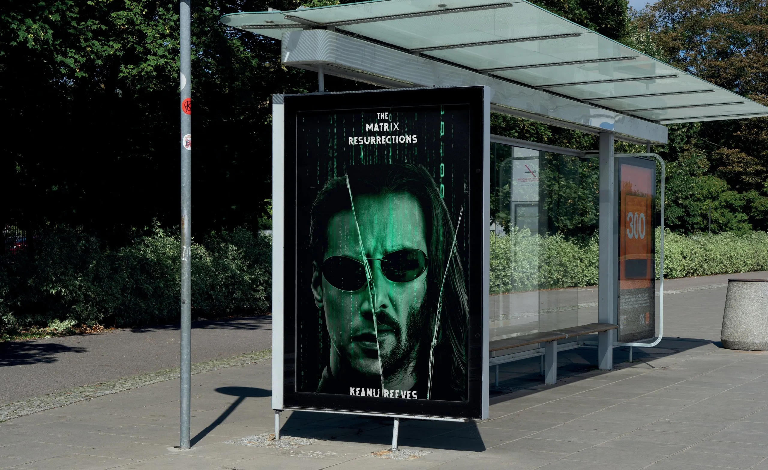 Yeşil dijital kod yağmuru üzerinde 'The Matrix Resurrections' afişi, bir otobüs durağı panosunda.